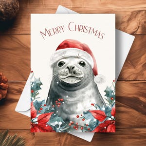 アザラシのクリスマス カード、サンタの帽子と赤いポインセチアのガーランドを身に着けている、ホッキョクアザラシの海の生き物のホリデー ギフト、水彩画のイラスト