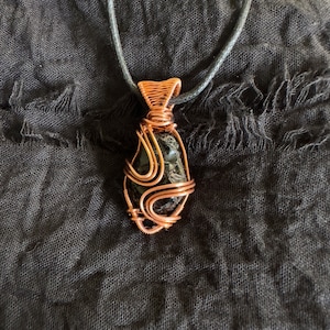 May include: A black gemstone pendant wrapped in copper wire, hanging from a black cord.