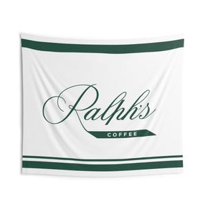 Può includere: Arazzo da parete bianco con bordo verde e la scritta "Ralph's Coffee" in corsivo. Il testo è verde scuro e l'arazzo ha un design semplice ed elegante.