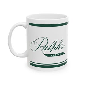 May include: White ceramic mug with a green stripe and the text "Ralph's Coffee" in a cursive font.