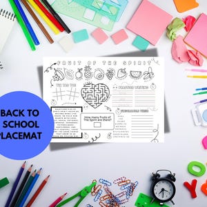 Op de afbeelding: Een witte placemat met de tekst "FRUIT OF THE SPIRIT" en "BACK TO SCHOOL PLACEMAT". De placemat bevat illustraties van fruit, een doolhof, boter-kaas-en-eieren en schrijfopdrachten. Schoolspullen omringen de placemat.