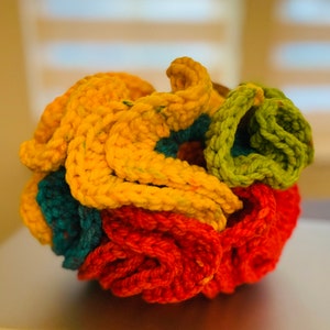 May include: A colorful, crocheted sphere featuring vibrant hues of yellow, orange, teal, and green. The handmade item has a textured, knotted appearance, with the yarn creating a three-dimensional, rounded shape. The craft item is likely a decorative piece or a unique home accent.