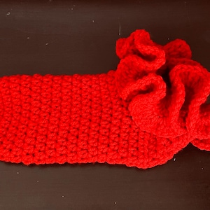May include: A vibrant red, handmade crochet slipper with a ruffled accent. The slipper is a solid, bold red color and appears to be made of soft yarn. The ruffled accent adds a decorative touch to the slipper.