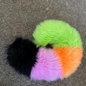Puede incluir: Una cola esponjosa multicolor con un pomp&oacute;n negro en el extremo. La cola est&aacute; hecha de piel sint&eacute;tica y es verde, naranja y rosa.