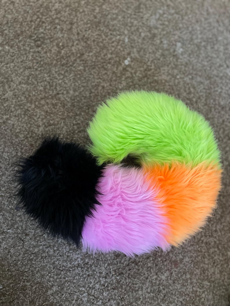 Puede incluir: Una cola esponjosa multicolor con un pomp&oacute;n negro en el extremo. La cola est&aacute; hecha de piel sint&eacute;tica y es verde, naranja y rosa.
