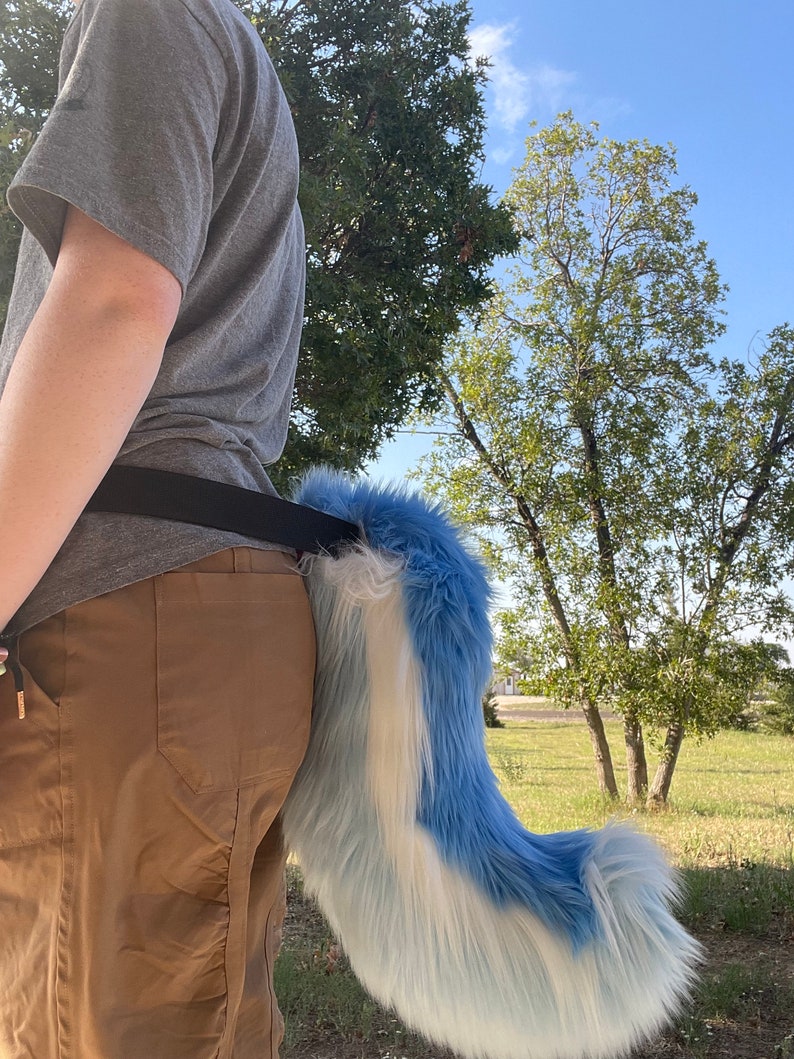 Puede incluir: Una cola esponjosa azul y blanca con una punta blanca, unida a un cintur&oacute;n negro que se lleva alrededor de la cintura.