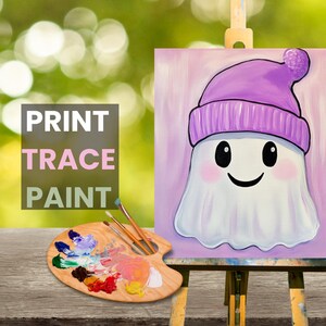 Puede incluir: Una pintura de un fantasma con un sombrero morado. El fantasma tiene una cara sonriente con ojos negros y mejillas rosadas. La pintura est&aacute; en un caballete de madera y hay una paleta de pintura con varios colores de pintura sobre una mesa de madera.