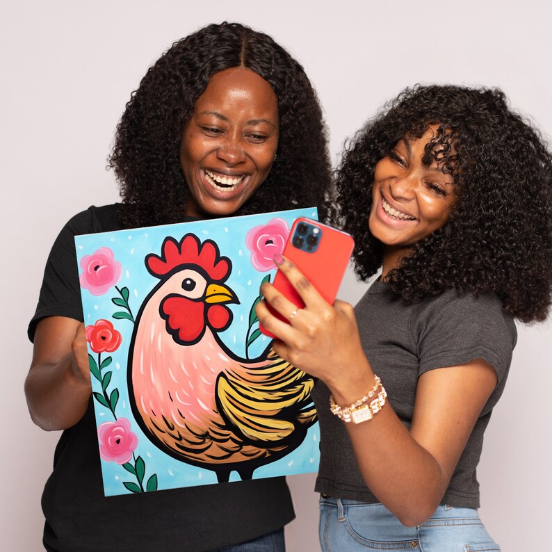 May include: Two people are smiling and holding a painting of a rooster with a pink and yellow body, red comb and wattle, and a blue background with pink flowers. The person on the left is holding the painting and the person on the right is holding a red phone.