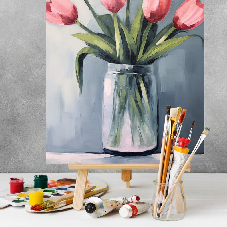 May include: A painting of a bouquet of pink tulips in a clear glass vase on an easel. The vase is sitting on a wooden surface. There are paintbrushes and paint tubes in the foreground.