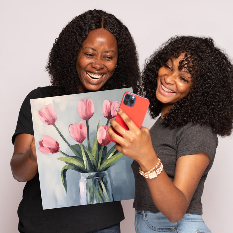 May include: Two people are looking at a painting of pink tulips in a glass vase. The painting is on a canvas and the people are smiling.