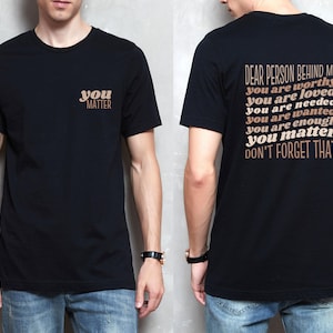 May include: A black t-shirt with the text "you matter" on the front and the text "Dear person behind me you are worthy you are loved you are needed you are wanted you are enough you matter don't forget that" on the back.