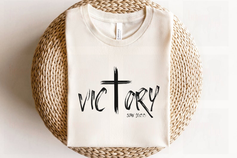 May include: A white t-shirt with a black cross and the word "VICTORY" written in a brushstroke font. The text "JOHN 16:33" is written below the word "VICTORY".