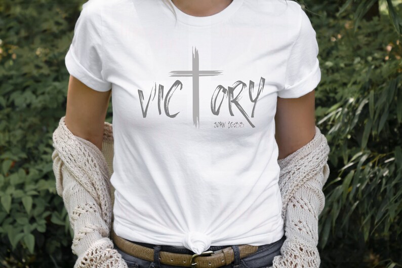 May include: White t-shirt with a gray cross and the word "VICTORY" in a brushstroke font. The text "John 16:33" is written below the word "VICTORY".