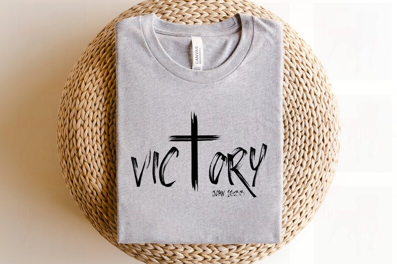 May include: A gray t-shirt with a black cross and the word "VICTORY" written in a bold, stylized font. The text "JOHN 16:33" is written below the word "VICTORY".