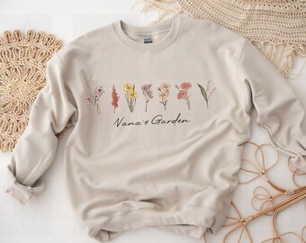 May include: A beige sweatshirt with a floral design and the text "Nana's Garden" printed on the front.