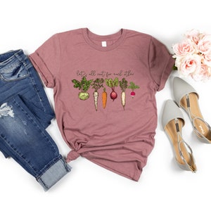 May include: A mauve t-shirt with a graphic of various vegetables and the text "Let's all root for each other".