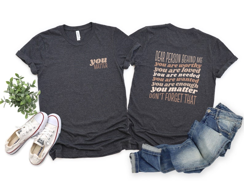 May include: A dark heather grey t-shirt with the text "you matter" on the front and the text "Dear person behind me you are worthy you are loved you are needed you are wanted you are enough you matter don't forget that" on the back.