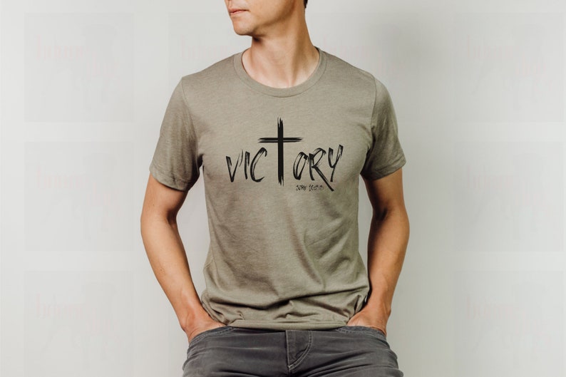 May include: A khaki t-shirt with a black graphic design of a cross and the word "VICTORY" with the text "Song of Songs 2:14" underneath.