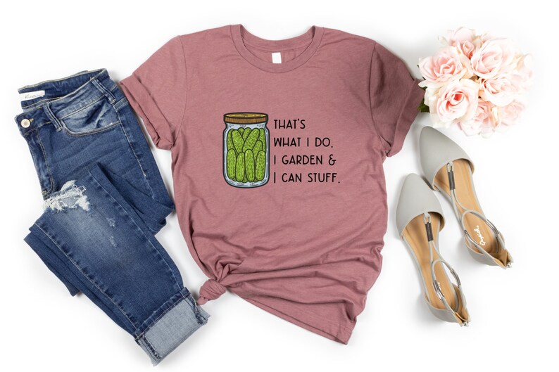 May include: A mauve t-shirt with a graphic of a jar of pickles and the text "That's what I do. I garden & I can stuff."
