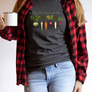 May include: A dark gray t-shirt with a graphic of vegetables and the text "Let's all root for each other".