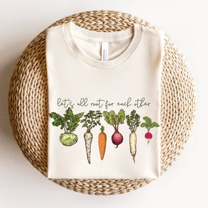 May include: A white t-shirt with a green, red, and orange illustration of various vegetables and the text "let's all root for each other".