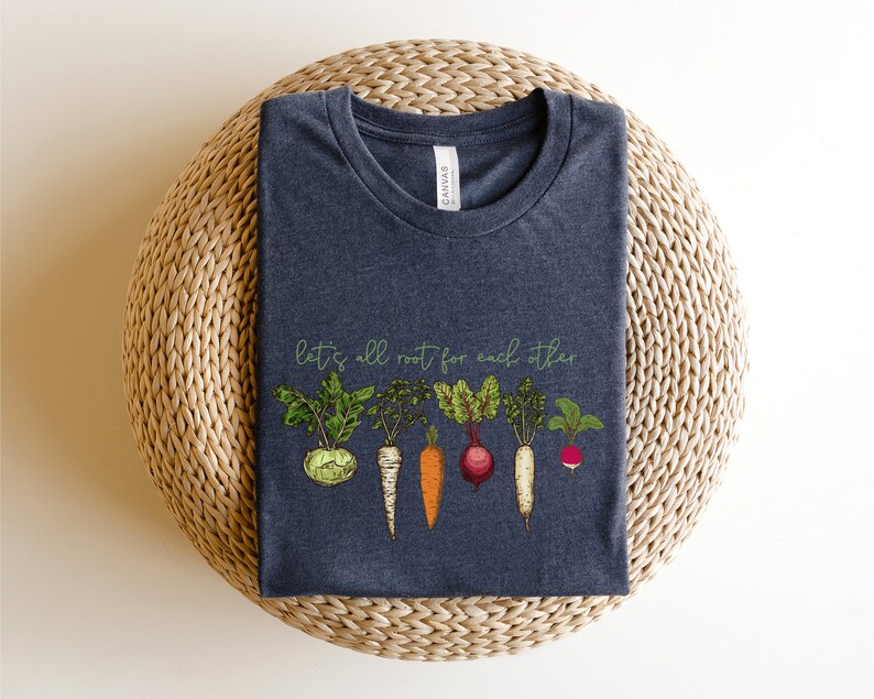 May include: A dark heather grey t-shirt with a graphic of various vegetables and the text "let's all root for each other".