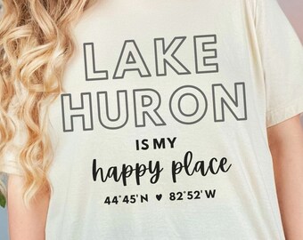 May include: A beige t-shirt with black text that reads "LAKE HURON IS MY happy place 44°45' N ♥ 82°52' W"