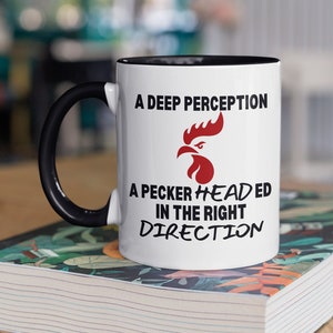 May include: White ceramic mug with a black handle and black rim. The mug has a red rooster graphic and the text "A deep perception, a pecker headed in the right direction."