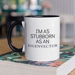 May include: White coffee mug with a black handle and black rim. The mug has the text "I'm as stubborn as an eigenvector" printed in black.