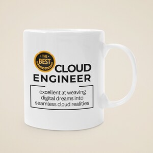 Peut inclure: Une tasse en céramique blanche avec un design noir et or. La tasse porte l'inscription "The Best Cloud Engineer" et "excellent at weaving digital dreams into seamless cloud realities".