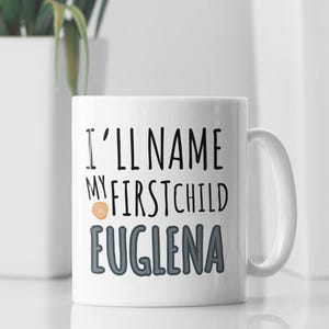 May include: White ceramic mug with a black and grey design. The mug says "I'll name my first child Euglena".