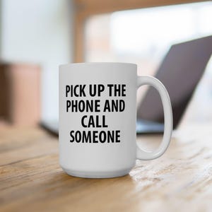 May include: White ceramic coffee mug with black text that reads "Pick up the phone and call someone".