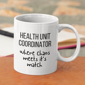 May include: White ceramic coffee mug with black text that reads "Health Unit Coordinator where chaos meets it's match".