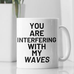 May include: White ceramic mug with black text that reads "You are interfering with my waves".