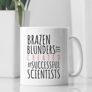 May include: White ceramic coffee mug with black text that reads "Brazen Blunders Are Created By Successful Scientists". The word "Created" is in pink.