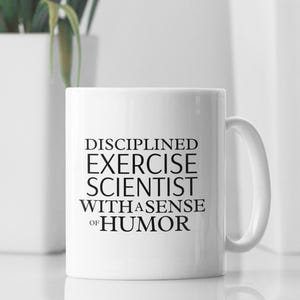 May include: White ceramic coffee mug with black text that reads "Disciplined Exercise Scientist with a Sense of Humour".