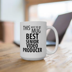 May include: White ceramic mug with black text that reads "This must be my mug best senior video producer".