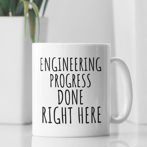 May include: White ceramic mug with black text that reads "Engineering Progress Done Right Here".