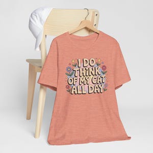 Peut inclure: Un t-shirt de couleur corail avec un imprimé graphique de fleurs et le texte "I DO THINK OF MY CAT ALL DAY".