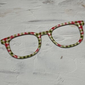 May include: A pair of round, red and green checkered glasses with a white background.