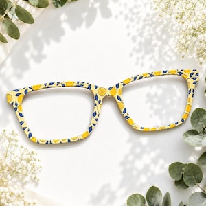 May include: Eyeglass frames featuring a repeating pattern of yellow lemons and dark blue leaves against a light cream background. The frames have a rectangular shape with rounded edges, showcasing a vibrant fruit-inspired design throughout.