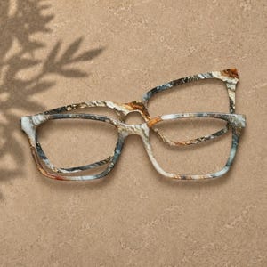 May include: A pair of eyeglasses featuring a rectangular frame with a marbled pattern in shades of brown, gray, white, and black. The frame has a smooth finish and a distinct multi-colored swirl design throughout the entire structure of the eyewear.