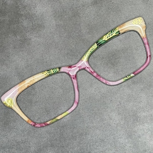 May include: A pair of pink and gold eyeglasses with a floral pattern. The glasses have a rectangular shape and are made of plastic.