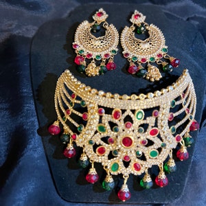 Puede incluir: Un conjunto de joyas dorado que incluye un collar y pendientes a juego. El collar y los pendientes están adornados con cristales transparentes y piedras preciosas rojas y verdes. Los pendientes tienen un diseño de araña y el collar tiene un patrón floral.