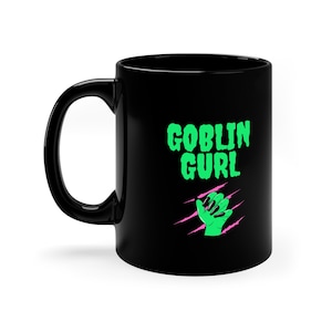 May include: Black ceramic coffee mug with a green and pink graphic of a hand with long nails and the text "GOBLIN GURL" in green.