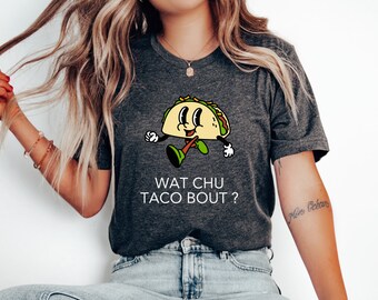 May include: Dark gray t-shirt featuring a cartoon taco character with a smiling face, arms, and legs. The text "WAT CHU TACO BOUT ?" is printed below the taco. The shirt is a casual, everyday wear item.