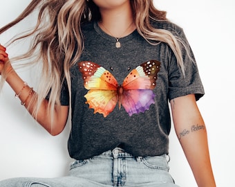 May include: A dark grey t-shirt with a colorful watercolor butterfly graphic. The butterfly has shades of orange, yellow, pink, purple, and brown.