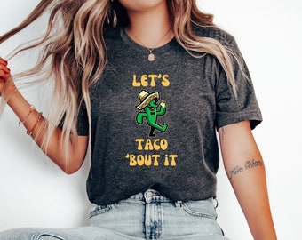 May include: A dark gray t-shirt with a green cartoon character wearing a sombrero and holding a taco. The text "Let's Taco 'Bout It" is printed in yellow on the shirt.