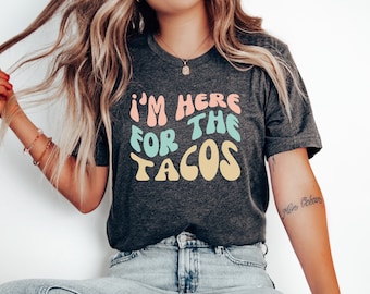 May include: A dark grey t-shirt with the text "I'm here for the tacos" in a colorful, retro font.