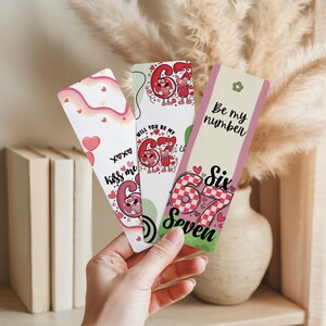 May include: Three decorative bookmarks with romantic themes. One bookmark has the text "Kiss me" and "XOXO" with hearts. Another says "Will you be my 67?" The third bookmark says "Be my number" and "Six Seven".